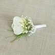 A single white orchid boutonniere rests gently on a softly textured, light beige fabric that looks like finely woven linen, its neutral oatmeal tone echoing the understated elegance of a Tufnell Park townhouse interior. At the heart of the piece, a pristine Phalaenopsis orchid bloom opens in a calm, sculptural curve, its broad, velvety petals glowing creamy white in even, natural light. In the centre of the flower, a hint of pale yellow in the throat adds warmth and depth, like a quiet candle flame, suggesting freshness and vitality perfect for a wedding morning near Tufnell Park station. Surrounding the orchid, airy clusters of white baby's breath scatter delicately in every direction, each tiny blossom forming a cloud-like halo that softens the silhouette and lends a romantic, almost ethereal quality. Slender strands of fine green foliage emerge from beneath the flowers, their feathery texture and vibrant colour adding a subtle wildness, as if just gathered from a leafy corner of nearby Hampstead Heath or a shaded garden off Fortress Road. The stems are neatly gathered and expertly wrapped with a smooth, bright white satin ribbon, pulled snug and tied into a small, impeccable bow that lies flat and ready to be pinned onto a lapel. The light catches the ribbon's gentle sheen, echoing the orchid's natural gloss and creating a cohesive, polished finish. This refined boutonniere feels perfectly suited for a groom or groomsman stepping out of a Tufnell Park terrace for a ceremony in a nearby church or registry office, embodying quiet sophistication, purity, and a sense of intimate celebration in the heart of North London.