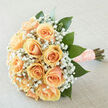 This bouquet is a portrait of tenderness, crafted around peach-hued roses whose creamy, swirled petals suggest soft silk under the fingertips. Clusters of airy baby's breath nestle between the larger blooms, their tiny white blossoms dancing to give the composition an ethereal, cloud-like surround. Lush, deep-green foliage provides a graceful scaffold, the glossy leaves punctuating the pastel palette and guiding the eye into a harmonious, rounded silhouette. The stems are carefully wrapped in a blush ribbon threaded with pearl details, the finish feeling both tactile and refined - a small, thoughtful touch that speaks to careful hand-tying and old-fashioned care. Bathed in diffuse daylight, the bouquet's gentle colours glow with warmth and restraint, evoking the composed optimism of a bride walking toward a new chapter. On the nose, the fragrance is clean and restrained: green-cut stems meet the soft, familiar sweetness of roses, with the barely-there powderiness of gypsophila completing the scent profile. As a florist serving Tufnell Park - a neighbourhood I know from Fortess Road to the green lanes near Dartmouth Park - I often recommend this arrangement for intimate ceremonies, vow renewals, or understated anniversary moments. Flowers Tufnell Park prepares each stem with attention to freshness and proportion, and this piece feels like a keepsake: delicate, enduring, and quietly celebratory, perfect for someone who values subtlety and heartfelt craftsmanship.