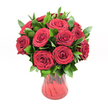 A lush, romantic bouquet of around a dozen deep red roses sits proudly in a translucent red glass vase, photographed against a pristine white background so every detail stands out clearly. Each rose is fully open yet still fresh, with velvety petals spiralling inward to a perfect centre, creating that classic, luxurious texture red roses are known for. The blooms are a rich crimson, almost ruby in places, and their saturated colour feels warm and passionate, like an intimate sunset over the rooftops of Tufnell Park. Between the roses, generous sprays of dark, glossy green foliage-likely ruscus-peek through, their smooth, pointed leaves adding contrast, structure, and a sense of natural abundance. The foliage frames the flowers rather than overwhelming them, guiding the eye gently around the rounded shape of the design. The red glass vase has a softly curving silhouette, slightly flared at the rim and narrowing towards the base, with a subtle ribbed or swirled texture that catches the light and echoes the curves of the petals. Because the glass is translucent, the red tone appears layered and alive, deepening where the stems gather. The even, bright studio lighting casts minimal shadow, ensuring the interplay between red blooms, green leaves, and the glass vessel is crisp and vivid. The overall feel is one of quiet yet unmistakable romance: a timeless rose arrangement that would suit a Valentine's Day surprise, an anniversary dinner on a Tufnell Park terrace, or any heartfelt gesture where pure, undiluted love needs no extra ornament. It is elegant, focused, and deeply expressive in its simplicity.
