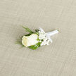 This wedding boutonnière is captured in intimate detail, resting on a pale, woven surface that recalls the calm, understated interiors of homes around Tufnell Park. At its centre, a creamy ivory rosebud slowly unfolds, each satin-smooth petal curving inward like a quiet promise spoken before guests arrive. Surrounding the rose is a delicate halo of fine baby's breath, each tiny white star-shaped flower softening the composition and lending it a gentle, cloud-like lightness. Slender, vivid green blades of ornamental grass weave and curl around the central bloom, adding a touch of movement and natural elegance that feels as relaxed and effortless as a stroll through Tufnell Park's tree-lined streets. The stem is expertly wrapped in shining white satin ribbon, tightly bound so that no rough edges show, ending in a neat and subtle bow that suggests care and thoughtful planning. The neutral background's subtle texture frames the arrangement without distraction, allowing the contrast between creamy petals, snowy gypsophila, and crisp greenery to shine. You can almost sense the coolness of the rose to the touch and imagine a faint, clean fragrance that hints at freshly cut flowers delivered early in the morning. Designed for a groom, best man, or cherished guest, this boutonnière suits intimate townhouse weddings and registry ceremonies near Junction Road just as well as grander celebrations. Its refined simplicity and precise craftsmanship echo the values of an experienced local florist, creating a piece that is modest in size but rich in meaning, ready to be pinned to a lapel and carried through an unforgettable day in Tufnell Park.