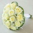 A high-angle, intimate photograph captures the essence of a luxurious bridal bouquet, crafted for a special celebration in Tufnell Park. Central to the composition is a tightly gathered array of ten to twelve fresh roses in hues of creamy white and pale yellow, each bloom at its freshest, petals tender and layered, conveying both innocence and quiet anticipation. Interspersed between the roses, clouds of baby's breath add an airy, delicate quality, their minuscule blossoms forming a luminous, ethereal mist enveloping the core of the bouquet. Subtle arcs of glossy deep green leaves sweep gracefully around the flowers, introducing contrast and framing the roses with natural elegance. The bouquet's stems are neatly trimmed and bound together with a pure white satin ribbon, its smooth texture and neat finish signifying a design made for confident hands on a wedding morning. The entire arrangement is set against a softly blurred, light background-perhaps a linen-draped table in a Tufnell Park home-focusing attention on the intricate layering of petals and verdant greenery. Exuding romance and sophistication, this bouquet captures the spirit of meaningful occasions, reflecting both the artistry and warmth of local florists who understand the beauty of celebration in North London.