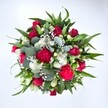 Viewed from directly above against a clean white backdrop, this generous bouquet forms a near-perfect circle of colour and texture, as if you were leaning over it on a kitchen table in a Tufnell Park townhouse. Deep crimson red roses sit at the heart, some still in tight bud, others gently unfurling to reveal velvety layers that suggest romance and quiet devotion. Around them, ruffled carnations in vivid fuchsia and ruby tones create a rich, almost frilly softness, their petals densely packed and full of movement. Clusters of small white spray chrysanthemums, with their daisy-like faces, tuck between the reds, scattering light and bringing a fresh, uplifting brightness. Threaded delicately through the arrangement is a fine mist of white gypsophila, or baby's breath, its tiny star-shaped blooms softening every edge and giving the bouquet a dreamy, cloud-like quality. Broad, pointed dark green leaves, likely from lilies or alstroemeria, radiate outward to frame the flowers, adding structure and a sense of strength beneath the romance. Nestled among them are rounded, silvery-green eucalyptus leaves, their matte texture and muted tone lending a modern, slightly wild feel, reminiscent of walks through nearby Hampstead Heath. The lighting is clear and even, letting every colour and curve stand out without harsh shadows, so the arrangement feels fresh from the florist's workbench. The overall mood is joyful yet elegant, a bouquet that could just as easily celebrate an anniversary on Campdale Road as brighten a friend's flat near Tufnell Park station. It speaks of love, appreciation, and well wishes, perfectly suited to birthdays, Valentine's surprises, or a heartfelt get well soon delivery across the neighbourhood.