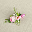This image shows an elegant boutonniere designed around a single, full-headed pink rose, its petals layered like satin, with a soft gradient that deepens towards the centre and fades to nearly sheer edges. Around it, a collar of blush alstroemeria blooms opens gracefully, each petal etched with faint yellow and rose-coloured markings that add subtle pattern and depth. Scattered between them are tiny clusters of white gypsophila, giving a frothy, starry texture that lightens the whole piece. Fine green foliage and slender grass-like fronds arc gently outward, bringing a fresh, garden-picked feeling, while firmer leafy greens provide structure and a crisp contrast in both colour and touch. The stems are neatly aligned and wrapped in a polished pink satin ribbon that gleams softly, holding everything in a clean, tapered finish ideal for pinning to a lapel. The boutonniere is photographed resting on a textured neutral fabric, whose weave and slightly matte surface make the pinks seem even cooler and more romantic. You can imagine this piece being crafted in a local Tufnell Park workshop, perhaps just off Fortess Road, and delivered fresh on the morning of a wedding or school leavers' celebration. The mood it creates is one of quiet celebration and thoughtful detail, the sort of floral touch that makes a walk through nearby streets to a registry office or venue feel more special, infusing the moment with gentle colour, fragrance, and a sense of carefully curated style.