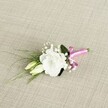 A single wedding boutonnière lies at a gentle diagonal on a softly textured, oatmeal-beige fabric that looks like finely woven linen, catching the light in subtle threads. At the heart of the design sits a fully opened white lisianthus bloom, its ruffled petals layered in soft curves, creating a cloud-like circle of ivory that feels both modern and timeless. Just below and to the left nestle two slender lisianthus buds in creamy pale green, their tips still closed, suggesting the quiet promise of a ceremony yet to unfold somewhere in Tufnell Park, perhaps just off Fortess Road. Around the main flower, tiny tufts of white gypsophila float like mist, filling the gaps with delicate dots of texture. Wispy, grass-like blades of foliage sweep outward towards the lower left, adding movement and a fresh, garden-picked feel, while a single, broader dark green leaf anchors the arrangement behind the bloom, giving depth and contrast. The stems are neatly gathered and wrapped in a smooth, fuchsia pink satin ribbon, tied into a small, jaunty bow that gleams against the muted background, adding a playful, celebratory splash of colour perfect for a groom's lapel. The lighting is soft and even, revealing every vein in the leaves and every fold of petal without harsh shadows, as if the piece had just been prepared by a local Tufnell Park florist for same-day collection before a registry office ceremony. The overall mood is fresh, romantic, and quietly joyful, ideal for weddings, civil partnerships, or school formals in the neighbourhood, capturing the elegance of white blooms with a bright, contemporary twist.