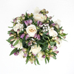 From a bird's-eye view, this sympathy bouquet rests on a spotless white background, appearing almost like a gentle, circular halo of flowers. At its centre, generous white roses open in silky layers, some in full bloom with their spiralled petals revealing creamy ivory and a faint peach warmth inside, others still slightly cupped, like hands holding quiet thoughts. Woven among the roses are purple alstroemeria buds, slender and slightly arching, their tightly closed petals shaded from deep lavender at the tips into fresh green and soft pink near the stems. A few buds look as though they might open with the next change of light, hinting at delicate stripes beneath. Fine sprays of baby's breath float between the larger flowers, each tiny white blossom creating a whisper-soft haze that lightens the arrangement and adds a dreamy, cloud-like texture. Encircling the blooms, lush greenery fans out in layered arcs, the deep green leaves smooth, supple, and gently reflective under the light, giving the bouquet structure and an organic, garden-like feel. The colours remain calm and reassuring-white, cream, purple, and green held in quiet harmony-echoing the kind of understated beauty you might find in a well-kept Tufnell Park doorstep display or a hidden courtyard near Kentish Town. It feels like a design created for someone sitting in a peaceful living room overlooking local rooftops, needing a floral gesture that offers support without drama. The bouquet invites a slow, reflective gaze, ideal for honouring memories and bringing a sense of soft, living presence to a farewell or condolence setting.