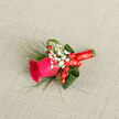 This boutonniere presents a single hot pink rose as its radiant focal point, resting on a woven, neutral background that highlights every nuance of colour and texture. The rose is captured at that ideal stage between bud and full bloom, with plump, velvety petals unfolding in graceful spirals, creating a lush, romantic centre. Surrounding it, delicate sprays of white baby's breath add a cloud-like softness, each tiny bloom a gentle contrast to the rose's bold cerise hue. Tucked between the petals and filler flowers, glossy red hypericum berries provide a joyful burst of scarlet, their rounded forms echoing the curve of the rose and lending a playful yet refined touch suitable for weddings and formal events across Tufnell Park and nearby Kentish Town. Curved green aspidistra leaves embrace the design, wrapping around the flowers in smooth arcs that give the boutonniere a sculpted, contemporary silhouette. Slim blades of ornamental grass extend lightly from the base, adding a sense of lift and movement, as though caught in soft evening light drifting over nearby Dartmouth Park. The stems are neatly bound in a deep red ribbon, wound with care to create a polished handle that feels cool and satin-smooth in the hand. The overall effect is one of modern romance-bright yet balanced, intricate yet not fussy-perfect for a groom, best man, or prom guest stepping out onto the streets around Tufnell Park station. Crafted with a local florist's eye for detail, every petal, berry, and leaf is positioned to look fresh, flattering, and ready for the camera.