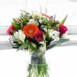 Gathered by a seasoned florist in Tufnell Park, this bouquet is a joyous celebration of fresh colour and emotional resonance. Dominating the scene, a brilliant tangerine Gerbera daisy bursts forth with a playful cheer, ringed by lush magenta and deep red roses-each bloom at a distinct stage, from tightly coiled bud to soft, passionate unfurl. White alstroemeria, their petals marked with fine pink stripes, cluster gracefully with star-like white chrysanthemums, lending a frothy, textured softness that uplifts the entire composition. At the edges, cream and pale yellow roses add a hush of subtlety, while delicate purple florets nod quietly from within, deepening the palette with understated calm-the way purple shadows linger at dusk along the quiet streets near Tufnell Park Station. The bouquet's stems are neatly arranged in a sturdy, clear glass vase, submerged in pristine water, anchored by sweeping, waxy Monstera-like leaves and an interplay of thin, lively greens. Sunlight, filtered through a local townhouse window, illuminates every petal and leaf, setting the whole arrangement aglow with the promise of joy, warmth, and connection. Perfect for birthdays, heartfelt congratulations, or simply brightening a home after a visit to Tufnell Park's local markets, this bouquet expresses the enduring beauty and welcoming spirit found in every hand-tied design created in this north London neighbourhood.