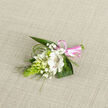 Set against a softly woven, light oatmeal fabric, this refined boutonniere appears as though it has just been laid down before being pinned to a lapel on a wedding morning in Tufnell Park. At its centre sits a luminous white alstroemeria-like flower, its petals opening generously and etched inside with delicate maroon-brown streaks that add depth and a hint of intrigue. Around it, smaller white blooms and buds cluster closely together, like quiet companions, their forms recalling campanula or lily-of-the-valley, each one poised between tight bud and gentle unfurling. Threads of white gypsophila scatter through the arrangement, their tiny blossoms catching the light and lending a misty softness that feels almost like breath on a cool day in nearby Hampstead Heath. On the left side, a vivid, cone-shaped column of bright green buds, reminiscent of ornithogalum, adds a fresh, architectural line and a burst of life-filled colour. Deep green leaves form a supportive cradle beneath, while fine arcs of slender grass sweep outward, tracing elegant lines that balance movement and stillness. The stems are gathered and wrapped in a glossy pink satin ribbon, tied into a neat bow that whispers of celebration-perfect for a wedding, prom, or anniversary gathering in a local Tufnell Park venue. The lighting is calm and even, revealing every nuance of petal texture, from the velvety softness of the main bloom to the crisp edges of the foliage. This small floral accent feels composed with great care, the kind of handcrafted buttonhole a local florist would prepare for a meaningful, once-in-a-lifetime moment.