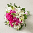 Resting on a subtly textured beige fabric, reminiscent of natural linen draped over a Tufnell Park dining table, this hand-tied bouquet feels like a snapshot of spring at its peak. At its heart, lush hot pink peonies are in full bloom, their many-layered petals spilling open in soft, generous ruffles. The colour is intense yet refined, a vivid raspberry-pink that instantly draws the gaze and suggests warmth, romance, and a touch of indulgence. Dancing between the peonies, white alstroemeria unfurl in graceful clusters, each slender petal brushed with faint speckles and stripes of rose and russet deep in the centre. These markings give the bouquet an intricate, almost painterly quality, like something you might carry from a wedding at a local Tufnell Park church to a reception along Brecknock Road. Slim, upright green buds break through the rounded shape of the design, their spiky silhouettes offering contrast and a sense of movement, as though new flowers are still on the verge of blooming. Around and beneath the blossoms, rich green foliage adds structure, the leaves curving and overlapping to create a sense of fullness and vitality. All of the stems are gathered carefully, aligned with precision and bound with a soft pink ribbon that winds tightly at the base, its satin finish catching the light in gentle highlights. The bouquet forms a pleasing dome that feels both intentional and natural, perfect for a bride walking through Tufnell Park's quiet residential streets or for same-day delivery as a joyful surprise to a home near the green spaces of local parks. The overall impression is one of freshness, celebration, and tender emotion.