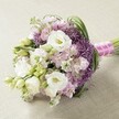 Artfully arranged and glowing in natural daylight, this lush bouquet celebrates the refined style of Tufnell Park weddings. Large, white lisianthus blossoms, their ruffled petals echoing with softness, are set against a medley of gentle pastel hues-light pink and lavender stock flowers add depth and airy motion to the composition. Spherical, deep purple Allium 'Star of Persia' peaks bring bold character and dramatic contrast, peeking from among the gently arching, bright green foliage that weaves throughout. The bouquet forms a rounded, elegantly elongated shape, suggesting movement and structure that mirrors Tufnell Park's blend of classic architecture and hidden gardens. Each stem is carefully bound in a sleek fuchsia satin ribbon, finished with a thread of delicate white pearls-a subtle, glamorous accent fit for special occasions on leafy Junction Road or community celebrations at local venues. Resting on a neutral, textured surface, every detail stands out: the layering of petals, interplay of colours, and artistry in the arrangement. The bouquet evokes romance, joy, and the vibrant yet understated elegance that makes Tufnell Park such a sought-after setting for memorable wedding days.
