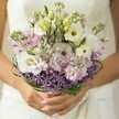 There is a gentle magic captured in this Tufnell Park bridal bouquet, a harmony of pastel tones and rich textures that evoke the quiet charm of local garden squares. Creamy white Lisianthus stand open, their softly pleated petals radiating warmth, each centre kissed with a hint of green-yellow-a subtle nod to life's unfolding. Around them, unopened buds and clusters of fragrant, light pink and lilac stock infuse the bouquet with a dreamy softness, layering scent and sensory delight. At the base, a ring of vibrant, starry purple Allium flowers adds structure and playful contrast, much like discovering bursts of wild colour along Dartmouth Park Hill. Slender, looping bear grass weaves around the bouquet, anchoring the design with a touch of modern sophistication. The bride's hands, with neatly polished nude nails, cradle the wrapped stems, offering an intimate sense of occasion. The softly blurred suggestion of a lace wedding dress in the background enhances the sense of romance and anticipation. Thoughtfully composed by local florists in Tufnell Park, this bouquet feels both timeless and freshly contemporary-an emblem of hope, joy, and beginnings, perfect for weddings in this spirited corner of North London.