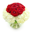 A clear, round glass bowl vase is centered against a stark white background, presenting a refined floral design that feels both classic and contemporary. Rising from the middle of the arrangement is a rounded crown of rich red roses, approximately nine to twelve blooms clustered closely together to create a smooth, domed silhouette. Each rose is at a lush, mid-bloom stage, with velvety petals spiralling outward in layered folds, some still slightly tight at the center and others gently opening to show deeper tones of crimson. Supporting this vivid cluster of roses is a generous base of creamy white hydrangeas, shaped into a full, almost spherical collar that envelops the lower half of the design. The hydrangea florets are small and densely packed, giving the impression of a soft, pillowy cloud from which the red roses emerge. The contrast between the intense red and the clean white is striking yet soothing, enhanced by the fresh green stems visible through the clear water in the vase. The stems curve naturally inside the glass, adding an organic sense of movement beneath the structured dome of blooms. The uninterrupted white backdrop keeps all attention on the flowers, highlighting their textures, colours, and the balance of the composition. This arrangement feels like it could be placed at the center of an anniversary dinner table in a flat off Fortess Road, or delivered as a heartfelt surprise to a loved one near Tufnell Park station. It conveys a quiet sense of celebration, devotion, and thoughtful craftsmanship, as though prepared that day by a local florist for same-day delivery around the Tufnell Park neighbourhood.