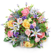 A lush, domed bouquet sits against a pure white backdrop, its dense, rounded silhouette casting a gentle soft-edged shadow and inviting a slow, sensory look. The composition is richly layered: soft garden roses in blush pink, warm buttery yellow, and creamy peach form the romantic heart, their velvety petals spiraling outward from tight buds to fully unfurled cups. Star-like clematis in pale lavender to near-white punctuate the roses, their open petals and bright yellow centres lending a light, airy geometry that lifts the arrangement. Architectural, steel-blue Eryngium (sea holly) thistles provide a striking contrast - spiky, metallic heads that add sculptural texture and a modern edge. Deeper purple lisianthus, some ruffled and some still coyly closed, weave through the flowers and deepen the colour story, while glossy red hypericum berries appear in small clusters, their round, jewel-like forms catching the light. A varied palette of foliage - broad glossy leaves, feathery green sprigs, and darker, burgundy-tinged filler leaves - nests the blooms, creating depth and a natural, garden-fresh base. The lighting is soft, even, and natural-looking, picking out petal translucence and the subtle sheen on berries and leaves. As a florist in Tufnell Park I picture this arrangement as a celebratory centrepiece for a riverside terrace near Dartmouth Park or a thoughtful gift delivered to a home off Fortess Road - it reads as joyful and elegant, balanced between wild garden charm and refined craftsmanship. It smells faintly of summer rain and greenery, and its harmonious contrast of soft pastels with jewel-toned accents makes it suitable for birthdays, anniversaries, or a warm thank-you.