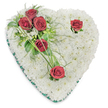 A heart-shaped funeral tribute crafted as a soft, white cushion of chrysanthemums fills the frame, the petals packed tightly to form a seamless, pillowy surface that suggests quiet comfort. The pristine white chrysanthemums read as purity and peaceful remembrance; their tiny, textured faces create a gentle ripple of light and shadow under soft overhead lighting. Against that serene white bed, a cluster of three deep red roses sits on the upper left curve, their petals fully opened and velvety to the eye, accompanied by glossy green leaves and delicate fern-like fronds that bring a whisper of woodland air. Two more single red roses punctuate the design-one poised near the upper right curve, the other resting toward the heart's pointed base-each framed by a few spare green blades and subtle white filler blooms that let the scarlet stand in solemn relief. A narrow emerald-green satin ribbon neatly traces the heart's perimeter, giving the arrangement a refined border and a quiet, dignified finish. The overall composition is lit to emphasize texture and depth: the chrysanthemums' softness, the roses' rich crimson, the cool sheen of the ribbon and foliage. Scent is implied-a light, classical perfume of rose over a clean chrysanthemum base-and the piece reads as a calm, respectful gesture of love and remembrance. This arrangement is the kind of traditional sympathy wreath families choose for funeral services in Tufnell Park and nearby Dartmouth Park, an emblem of condolence that speaks of enduring respect and tender memory.