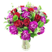 A sumptuous, rounded bouquet of deep red roses and magenta-purple carnations sits in a clear glass vase, described here as if placed on a white tabletop in soft morning light. The roses range from tight buds to gently unfurling blooms, their velvety, spiral petals catching highlights at the edges and suggesting a warm, romantic scent. Interspersed among them are lavish, ruffled carnations in a vivid fuchsia-leaning purple, each layered petal creating feathery texture and a lively contrast to the smooth rose cups. Bright, glossy green foliage - the broad leaves reminiscent of ruscus - fills the interior and base of the cluster, giving the arrangement a full, verdant silhouette, while slender sprigs of silvery eucalyptus lift the composition with cool, matte tones and a whisper of aromatic freshness. The stems are visible through the transparent vase, cut cleanly and gathered to create a dense, domed shape that reads as both abundant and carefully balanced. Against the pristine white background the reds and purples appear intensified, the greens acting as a cool foil that makes each bloom pop visually. The overall impression is celebratory yet refined, an arrangement suited to anniversaries, birthdays, or an affectionate surprise delivered across Tufnell Park or neighbouring Kentish Town. As a local florist would note, the tactile contrasts - velvet to ruffle to glossy leaf - invite touch; the bouquet reads as thoughtful, freshly made the same day, and gestures toward heartfelt congratulations or quiet devotion in a way that is both elegant and approachable.
