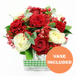 A single, abundant bouquet is captured in sharp focus against a plain white background, allowing the interplay of red, white, and green to command all the attention. At the heart of the design, velvety red roses and creamy white roses are massed together, their open blooms forming a rich tapestry of spiralling petals that feel both romantic and uplifting. The red roses bring depth and intensity, while the white ones offer a gentle, calming contrast, creating a balance that would suit both cosy flats and larger homes around Tufnell Park. Scattered throughout are countless tiny red filler flowers that resemble tinted baby's breath, their fine stems and clustered blossoms giving the arrangement a light, airy texture, like a soft red haze settling between the larger blooms. Shiny red hypericum berries punctuate the bouquet, round and smooth, providing a playful, almost jewel-like effect that catches the eye. Eucalyptus sprigs and varied greenery weave around and beneath the roses, introducing cool green tones and hints of silvery blue that suggest freshness and a subtle, herbal fragrance, much like the scent you notice when fresh flowers are delivered to a home near Tufnell Park Station. All of this is gathered into a clear, rectangular glass vase, placed centrally in the lower part of the image, its transparency revealing the straight, clean lines of the stems inside. A green and white gingham ribbon encircles the vase, adding homely charm and a touch of seasonal style, reminiscent of a well-loved kitchen or a festive table near Fortess Road. In the bottom right corner, a bright orange circular badge with bold white lettering clearly states VASE INCLUDED, highlighting that this elegant, ready-to-display floral piece arrives complete, perfect for romantic occasions, family gatherings, or simply adding warmth to an everyday North London evening.