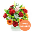 This photograph captures a lively, mixed bouquet that feels instantly celebratory, as though it has just been set down on a dining table in a Tufnell Park townhouse before friends arrive. The flowers are gathered into a clear rectangular glass vase, the stems visible through the water, and the bottom is wrapped with a light green and white gingham ribbon, giving a soft, welcoming note of domestic charm. Against a clean white backdrop, the colours appear vivid and fresh. Deep red roses form the emotional anchor of the design, their velvety, tightly furled petals suggesting both romance and care. Intermingled with them are red-orange carnations, whose ruffled heads add layers of texture and volume, creating a sense of abundance. Cheerful orange gerbera daisies, each with a bold dark centre, tilt forward and outward like playful faces, sending out warmth that could brighten a flat near Junction Road or a studio overlooking the railway lines. Clustered among these are plump lime-green button chrysanthemums, their small spherical blooms adding a cool, zesty contrast that keeps the palette feeling modern. Standing taller, white Oriental lilies provide a graceful vertical line; some have fully opened, revealing wide petals brushed with gentle pink along the centre veins, while others remain in smooth, tapered buds that hint at tomorrow's beauty. Glossy dark green leaves and airy sprigs of silver-green eucalyptus weave through the bouquet, framing the brighter blooms and giving depth and shape. At the lower right corner of the image, overlapping the vase, an orange circular label bears the message VASE INCLUDED in bold white uppercase letters, indicating that the glass container is supplied as part of the arrangement, ready for same-day delivery across Tufnell Park and neighbouring Archway or Kentish Town.