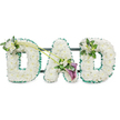A dignified, three-dimensional funeral tribute spelling out the word DAD, each letter built from hundreds of tightly packed, pristine white chrysanthemums and similar small white button blooms to form soft, cloud-like surfaces. The dense petals create a gentle, cushiony texture that reads as both comforting and solemn; you can almost sense the faint sweet, honeyed fragrance of the chrysanthemums mingling with the clean, delicate perfume of white freesia used as accents. Each letter is crisply outlined by an emerald-green satin ribbon that provides a precise, botanical edge against the snowy white faces, while a discreet dark support frame with horizontal bars is visible behind the letters, showing the piece is designed to stand upright at a service or graveside. Thoughtful floral clusters punctuate the composition: a small spray of white freesia and lush green foliage sits on the upper left curve of the first D, and the final D is mirrored with a compact cluster of the same white freesia and leaves on its upper right. Between the letters, two long arcing green stems carry an asymmetrical line of blooms that culminates near the base of the central A, where two deep purple calla lilies-trumpet-shaped and velvety-nestle among white flowers and glossy green leaves, giving a restrained contrast and focal depth. The photograph, taken against a clean white background with soft, even light, conveys respectful gravity and personal love, the kind of bespoke memorial we arrange for local families in Tufnell Park when they want a clear, heartfelt message of remembrance for a father.