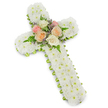 A visually serene and traditional funeral cross, photographed against a brilliantly white background with a soft drop shadow that reveals its three-dimensional form. The cross itself is built from hundreds of small, button-style white chrysanthemums tightly packed to form a plush, velvety surface-each tiny blossom contributing to an even, pristine field of white that reads of purity, peace, and gentle reverence. The perimeter of the cross is finished with a narrow lime-green trim that peeks out beneath the white blooms, a crisp ribbon-like border that defines the silhouette and adds a whisper of renewing colour. At the exact intersection of the upright and crossbar a concentrated bouquet becomes the focal point: several open, garden-style roses in sympathetic shades of soft blush pink, warm peach-cream and ivory are arranged with slender green fern fronds and feathery sprigs of pale lavender filler, their cool purple notes bringing a subtle contrast against the warm roses and pure chrysanthemums. The texture moves from the dense, cushiony body of button blooms to the softer, fragrant petals of the roses and the airy movement of the ferns, suggesting both dignity and tenderness. There is a faint suggestion of scent-clean green notes from the ribbon and fern, the heady, understated sweetness of roses-inviting a moment of reflection. As a sympathetic tribute commonly used at funerals, memorials and graveside services, this arrangement carries a quiet, faithful symbolism. A local florist might imagine it placed near the altar at a chapel in Tufnell Park or set carefully beside a headstone in nearby Dartmouth Park, offering comfort and a measured beauty in times of farewell.