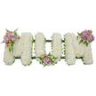 A reverent, three-dimensional funeral tribute carefully composed to spell the word MUM in bold capital letters, set against a pristine white backdrop that heightens the arrangement's quiet dignity. Each of the three letters - M, U, M - is densely carpeted with hundreds of small, snowy-white spray chrysanthemums or similar tiny white blooms, their closely packed petals forming a soft, cloud-like surface that invites a gentle touch. Against this field of white sit three delicate clusters of pastel-soft lavender and blush-pink-roses, each cluster chosen for velvety texture and subtle scent; one nestles on the upper left arm of the first M, another curves into the hollow of the central U, and a third rests on the upper right arm of the final M, creating a balanced, heartfelt punctuation to the composition. Fresh green foliage - slender fern fronds, lighter-green filler leaves and glossy greens - frames the blooms and provides depth, their serrated edges and varied tones giving a living contrast to the white surface. A darker, mossy or ribbon-wrapped structural base peeks beneath the flowers, outlining the letter shapes and lending the tribute a stable, sculptural silhouette suitable for standing at a funeral or graveside. The overall effect is one of calm and respect: the white chrysanthemum surface speaks of purity and remembrance, while the lavender and pink accents bring warmth and affection, making this a comforting, personal memorial for a beloved mother, arranged with the considered care of an experienced florist familiar with funerals and wakes in the local London neighbourhood.