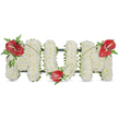 A dignified three-dimensional tribute spells the word MOM in large, freestanding letters formed from hundreds of small, pristine white spray chrysanthemums. Each bloom is chosen for fullness and set close together so the surface reads like a soft, cloud-like cushion: matte petals, tiny yellow eyes peeking through, and a quiet, powdery scent that speaks of calm and reverence. The dense white faces of the flowers are held by a subtle dark-green structural frame that shows only at the edges, giving the letters solidity without distracting from their purity. To break the plane of white and introduce a note of warm intimacy, three glossy red anthuriums are artfully placed-one anchoring the upper left of the first 'M', one resting at the base of the central 'O', and the last adorning the upper right of the final 'M'. Each anthurium shows its smooth, waxy heart-shape and a pale yellow-white spadix, their reflective surfaces catching soft daylight and drawing the eye. Around the red blooms, feathery fern fronds and broader deep-green leaves cradle the spathes, while thin, arching blades of grass or stems sweep gently across the letters to visually tie the three accents together. The overall palette of satin white, glossy scarlet, and shadowed green reads as both classic and tender, a sympathetic expression intended for a mother's memorial. The piece feels composed in natural daylight-gentle highlights, soft shadows-and is the kind of arrangement a local florist would place at a wake or graveside, offering a clear, heartfelt message of love, dignity, and remembrance.