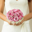 In this intimate bridal scene, the bouquet appears as a flawless sphere of blush pink roses nestled among clouds of white gypsophila, resting securely in the bride's hands against the backdrop of an elegant lace gown. Each rose is in peak bloom, with layered petals unfolding in soft spirals, tinted in shades that move from dusky rose blush at the heart to a gentle ivory kiss at the edges. The baby's breath threads through and around the roses, its tiny white flowers creating a misty, lace-like frame that echoes the gown's delicate detailing. The composition is carefully balanced, every rose placed so the bouquet feels both full and airy, not too tight, yet beautifully complete. In the gentle daylight-much like the soft light that filters through a Tufnell Park terrace on a quiet afternoon-the pinks, whites, and fresh green stems glow with understated elegance. You can almost sense the cool smoothness of the stems under the bride's fingers, and the feathery touch of gypsophila brushing lightly against her hands. The mood is one of quiet joy and serene confidence, the kind of feeling you might notice before a ceremony at a local church or a reception tucked away near Tufnell Park's leafy streets. Though the image is still, it holds the suggestion of movement: steps down an aisle, a shared smile, the rustle of lace. This bouquet stands as a gentle symbol of lasting affection, crafted with a florist's eye for harmony and a deep respect for tradition.