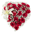 A meticulously crafted heart-shaped floral display sits against a pure white backdrop, its silhouette defined by a dense, luxurious carpet of deep crimson roses. The roses range from tight, velvet-wrapped buds to fully opened blossoms, their layered petals catching soft studio light and casting gentle, satin shadows that deepen the red into rich, romantic tones. Cloud-like clusters of tiny white baby's breath (Gypsophila) are woven throughout and along the heart's edges, their feathery sprays creating a delicate halo that lightens the composition and lends an airy, tender texture between the larger blooms. Nestled in the upper-left curve, a single, sculptural white lily opens with broad, pristine petals and a faint creamy yellow wash near its throat; its yellow stamens provide a subtle, warm punctuation against the cool white and passionate red. The arrangement reads as both passionate and refined, a careful balance of weight and breath that invites the eye to travel from the dense centre outward to the soft, lacy borders. There is the implied scent of sweet rose perfume tempered by the green, clean note of the lily, suggesting an intimate bouquet meant to be both seen and gently inhaled. The composition speaks of deliberate craftsmanship-precise shaping, considered negative space, and a commitment to classic romance-appropriate for anniversaries, Valentine's gestures, or a sophisticated sympathy tribute. Picture this delivered locally to a home on Tufnell Park Road or placed on a mantel near Dartmouth Park: a floral declaration shaped to be held close to the heart and remembered long after the blooms soften.