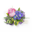 A beautifully crafted floral corsage or boutonniere photographed against a clean white background, the kind of small work of art I make for weddings and proms in Tufnell Park. At the center sits a single elegant rose whose petals graduate from a soft lavender-pink at the heart to a vivid fuchsia at the outer edges; its velvety curves suggest a gentle, powdery scent when held close. To the right, a tight cluster of indigo-purple florets - reminiscent of hydrangea - offer a cool counterpoint, each tiny bloom revealing a bright blue and lime-yellow-green center that catches the light like tiny beacons. The blooms are cradled by a careful mix of greenery: broad variegated ivy leaves with deep emerald centres and sunny golden-yellow margins form a classic frame, while slender, silvery-green foliage-suggestive of lavender or sage-softens the silhouette. A sculptural curled leaf, striped green and cream, adds an elegant twist and modern line. Wispy asparagus-fern sprigs thread through the composition, bringing breath and movement. Underlying it all, an intricate dark purple mesh peeks from beneath the flowers, creating depth and a contemporary shimmer against the white backdrop. At the lower right, a short strand of lustrous white pearls suggests a wristlet or decorative attachment, catching the eye with polished contrast. The piece reads as intimate and celebratory, designed to be pinned to a lapel or worn on the wrist for a Dartmouth Park or Junction Road celebration, a small talisman of care and ceremony for someone stepping out from Tufnell Park on a meaningful day.