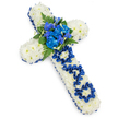 A large, symbolic funeral cross is shown on a bright white background, its presence both strong and tender. The cross is entirely paved with pristine white spray chrysanthemums, each bloom small but full, packed closely together to create a soft, enveloping surface that feels almost like snow freshly settled. Around every edge runs a border of royal blue satin ribbon, gently pleated and slightly raised, giving definition to the shape and adding a regal, respectful tone. Where the vertical and horizontal arms meet, a striking arrangement of rich blue flowers forms the heart of the design: lush, frilled blue carnations combine with more delicate, elongated blue blossoms reminiscent of delphiniums or orchids, their lines adding a sense of height and gentle movement. These blue flowers are interwoven with deep green fern fronds and other foliage, whose textures and shades of green bring a natural balance to the cool colour palette. On the vertical stem of the cross, the word DAD is carefully written using loops and folds of the same royal blue ribbon, the letters secured into the chrysanthemum base so they sit clearly but harmoniously within the design. The clean, uncluttered background and soft, even lighting ensure the focus remains solely on this poignant floral tribute. It feels like a piece that could be carried through a quiet Tufnell Park street to a nearby chapel or placed thoughtfully at a graveside, a deeply personal expression of love, loss, and gratitude for a cherished father, created by a local florist who understands the importance of both symbolism and tenderness in times of mourning.