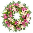 A luxurious circular wreath designed as a sympathy or funeral tribute is displayed against a plain white background, making the intricate floral work the sole focus. The wreath forms a flawless ring, densely covered with fresh flowers in a warm palette of pinks and creams. At its heart are numerous roses in rich magenta, vivid fuchsia, and soft blush pink, their petals unfolding in graceful spirals. Some rose heads appear tight and youthful, while others are fully blown, revealing plush, layered centres that suggest both abundance and tenderness. Woven through and between the roses are large double lilies, their generous petals opening outwards in shades of creamy white, pale pink, and delicate peach, creating soft star-shaped accents around the wreath. Here and there, unopened lily buds in bright lime-green rise from the foliage, hinting at blooms still to come and subtly symbolising ongoing life and remembrance. The flowers rest on a luxuriant bed of greenery: feathery fern fronds provide a gentle, airy frame at the outer edge, while broader, glossy dark green leaves fill any spaces and lend structure. The contrast between the deep greens and the warm rose and lily tones gives the wreath a rich, balanced appearance. This design carries a calm, reflective mood, ideal for expressing sympathy at funerals, memorials, or celebrations of life in Tufnell Park and the surrounding North London neighbourhoods. It feels like something a caring local florist would create for a family saying their last goodbye, a circular embrace of colour and texture that quietly honours a life lived and loved.