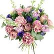A luxurious hand-tied bouquet sits suspended against a stark white background, every bloom and leaf standing out with crisp clarity. The eye is first drawn to the lush garden roses at the centre, their petals unfurling in spirals of blush pink, dusty mauve, and antique rose, each flower like a small, perfectly formed rosette. Nestled around them, ruffled carnations billow outward, with creamy, pale-pink centres melting into deeper tones of rose, fuchsia, and plum along their frilly edges, creating a sense of movement and softness. Deep, indigo-blue blossoms, some still tight like tulip buds, add pockets of dramatic colour, while a single open royal blue anemone with a dark, almost black heart sits near the lower edge, lending a striking focal point to the design. Wisps of lilac and pale lavender stock weave up through the bouquet on slender stems, their many small blooms offering lightness, height, and the suggestion of a sweet, powdery aroma. All of this is framed by a generous collar of foliage: cool, silvery-green eucalyptus discs alternate with richer, darker green leaves, suggesting the fresh, green scent you notice when you first walk into a local florist along Fortess Road. The stems gather neatly at the base, clearly visible and freshly cut, as if the bouquet has just been finished and is ready for same-day delivery around Tufnell Park, Gospel Oak, or Dartmouth Park. The overall mood is tender and elegant, a soothing blend of pinks, purples, blues, and greens that would suit an anniversary, a thoughtful thank-you, or a quiet gesture of comfort.